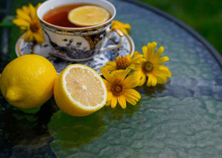 Cup of lemon tea with fresh lemons and yellow flowers, health benefits of lemon